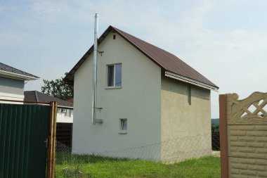 Kahverengi kiremitli çatının altında yeşil çimenler ve çitler içinde büyük gri bir ev.