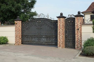 a black iron gate with a forged pattern and a closed door against the wall of a fence made of brown bricks and gray concrete on the street clipart