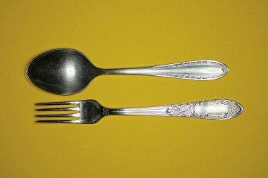 İki gri metal çatal ve kaşık sarı bir masada yatıyor.