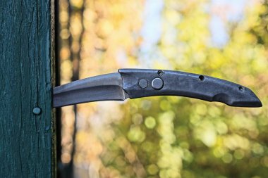 Eski, gri, katlanabilir bir bıçak. Dışarıdaki duvarda yeşil ahşap bir tahta.