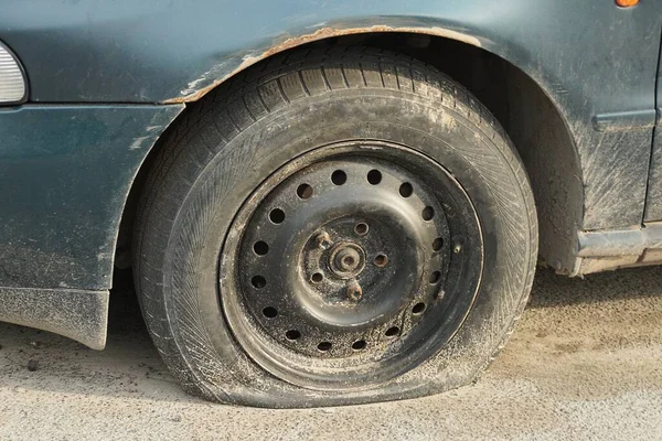 街上一辆绿色轿车上的一个黑色扁平轮胎和灰色沥青混合在一起 — 图库照片
