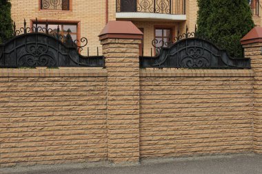 Gri asfalt üzerinde, sokakta bir tuğla çitin kahverengi duvarının bir parçası.