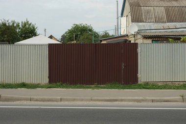 Büyük metal kapalı kahverengi kapı ve sokaktaki gri demir çitin bir kısmı