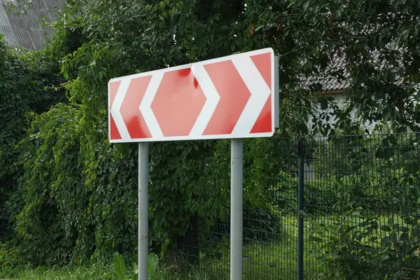 一个大路标在柏油路旁边的绿草上 用红色的白色箭头转向 — 图库照片