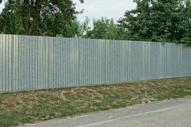 Kırsal bir sokakta, yeşil çimlerde, gri, uzun demir bir çitin bir parçası.