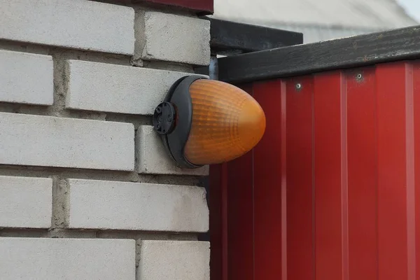 一个橙色的塑料信号灯挂在街上篱笆的白色砖墙上 — 图库照片