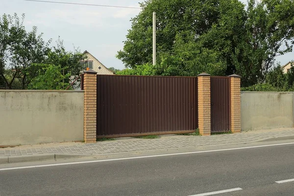 柏油路旁边街道上灰色篱笆墙上的褐色铁门和门 — 图库照片