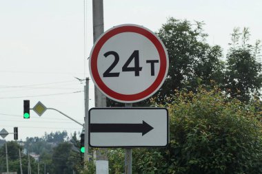 24 ton ağırlığı sınırlayan iki yol işareti ve yeşil bitki örtüsünün arka planına karşı sokakta bir ok.