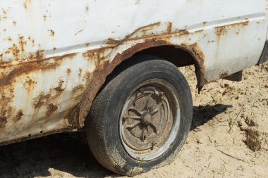 Kahverengi pas içinde beyaz eski bir yolcu vagonunun parçası. Sokakta kumun üzerinde siyah bir tekerlek var.