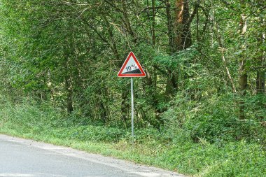 Caddedeki bir sütunun üzerindeki yol tabelası yamaç ve yeşil bitki örtüsü.