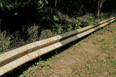 Gri çizgili paslı uzun metal bariyer yol boyunca yeşil bir bitki örtüsünün üzerinde.