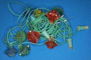 Eski renkli bir Noel çelengi yığını içinde yeşil bir elektrik teli mavi bir masada yatıyor.