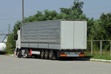 Asfalt yolda konteynırı olan büyük gri bir kamyonun parçası.