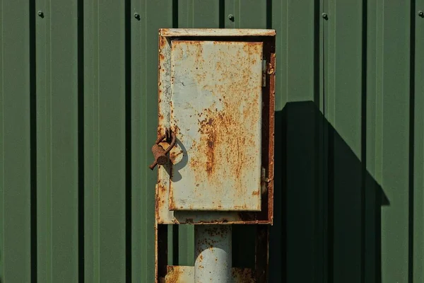 一个褐色铁锈灰色金属盒 杆子上有电线 外面有一个绿色铁栅栏 — 图库照片