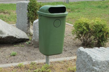 Yeşil plastik bir vazo parktaki çimlerde duruyor. Büyük gri taşların arasında.