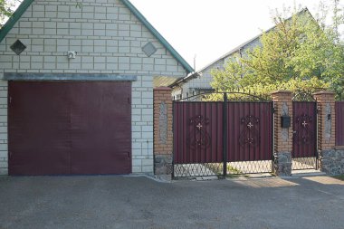 Caddedeki tuğladan bir garajın ön cephesi. Kahverengi metal bir kapının ve siyah işlemeli demir desenli bir kapının yanında.