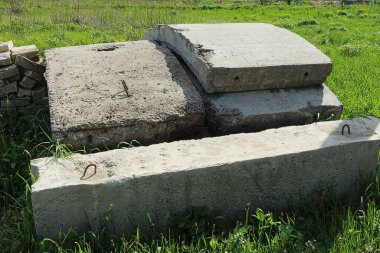 Eski gri beton levhalar sokakta yeşil çimlerde yatıyor.