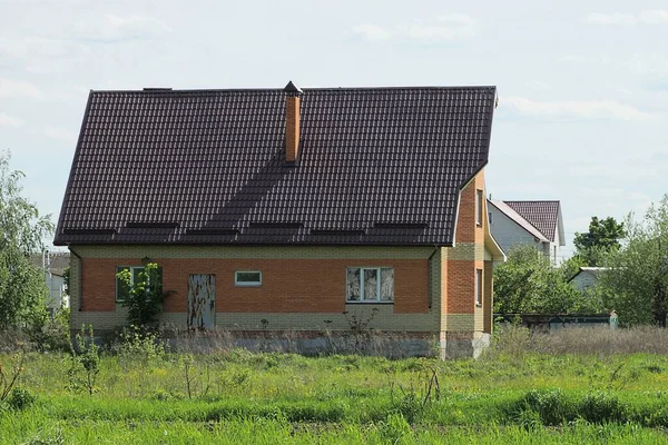 Caddedeki yeşil çimlerin altında fayanslı çatı altında pencereleri olan büyük kahverengi tuğlalı özel bir evin ön cephesi.