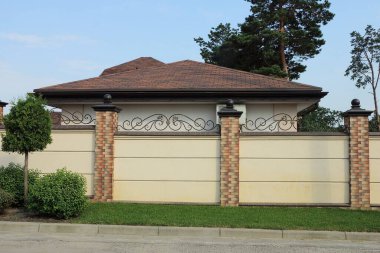 Gri beton ve kahverengi tuğlalardan yapılmış bir çitin duvarında yeşil çimlerin üzerinde.