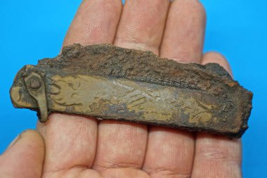 Kahverengi paslı demir bıçaklı eski yeşil bakır bir bıçak mavi arka planda, parmaklarda yatıyor.