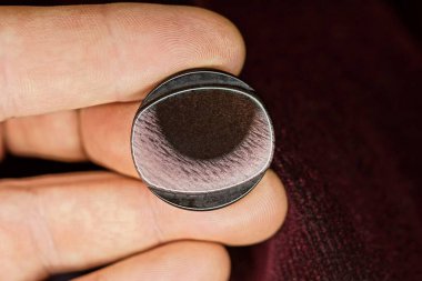 Elin üzerindeki parmaklar elbisenin kumaşında büyük bir plastik kahverengi düğme tutuyor.