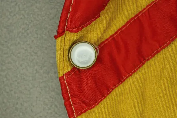 Kırmızı sarı kumaştan yapılmış ceketin bir parçası. Gri bir masada tek bir plastik beyaz düğme var.