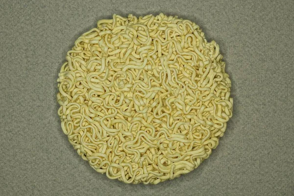 one piece of dry round yellow vermicelli lies on a gray table