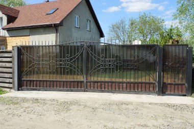 Kırsal bir sokakta dövülmüş demir desenli büyük siyah metal kapı ve kapı.