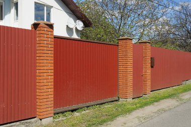 Kırsal bir sokakta demir ve tuğladan yapılmış bir çitin duvarındaki kırmızı metal kapı ve kapı.