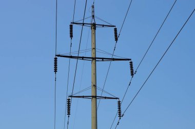 Uzun, gri beton bir sütun. Sokakta mavi gökyüzüne karşı elektrik kabloları var.