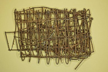 Paslı demir çubuklardan yapılmış eski kahverengi bir ızgara parçası sarı bir masanın üzerinde duruyor.