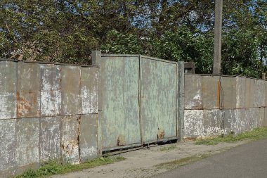 Pas içindeki eski yeşil metal kapı ve kırsal bir sokakta gri demir duvar çitinin bir kısmı