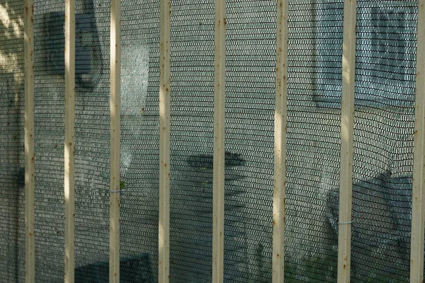 布の緑のメッシュを背景にフェンスの中の茶色の金属棒の質感 — ストック写真