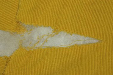 Eski bir ceketin sarı kumaşında beyaz pamuklu büyük bir delik.