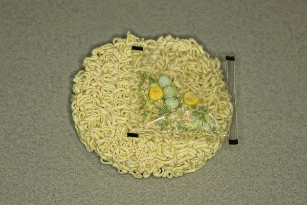 plastic bag with seasoning and a yellow piece of round dry vermicelli lies on a gray table