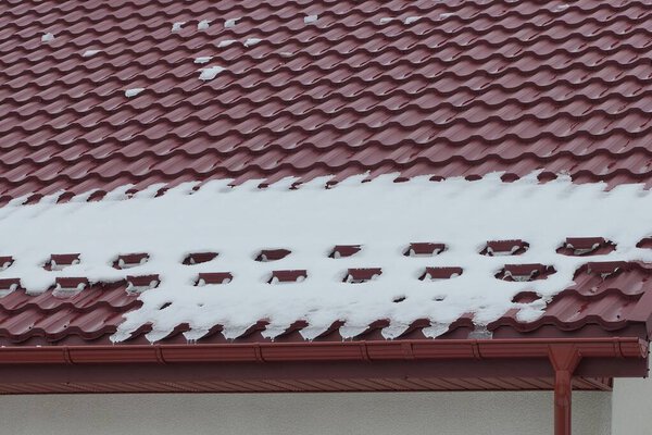 part of a roof made of red metal tiles under white snow on a winter street