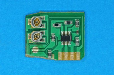 Eski yeşil elektronik bir mikro devrede siyah ve gri parçalar mavi bir masada yatıyor.