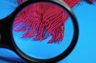 siyah büyüteç mavi masada kırmızı yün şalı büyütüyor