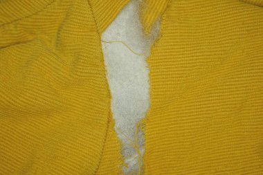 one big hole with white cotton wool on the yellow fabric of an old jacket