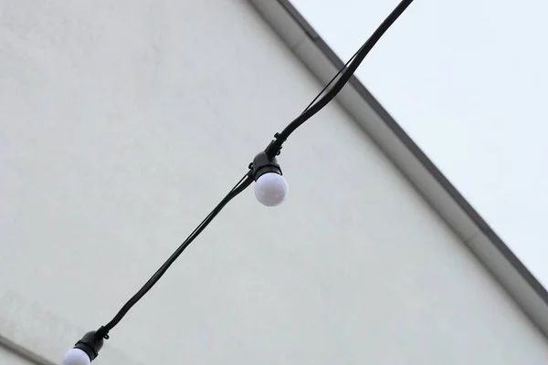 街上一根黑色电线上的一个小的白色灯泡靠着灰色的墙 — 图库照片
