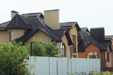 large brown private house with windows and an open iron balcony behind a gray metal fence against the sky