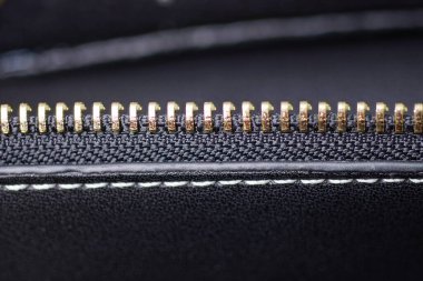 part of a black leather bag with a seam and an open zip with brown metal teeth on the fabric