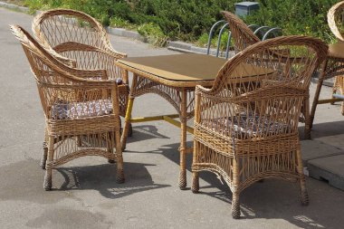 Kahverengi hasır ahşap koltuklar ve sokaktaki gri asfaltta bir masa standı.