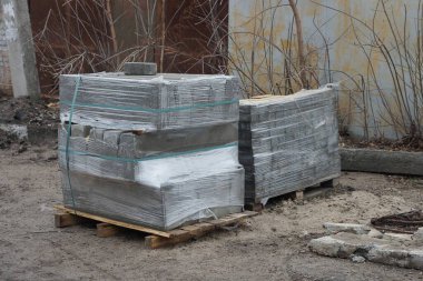 İki kare kutu plastik ambalajda asfalt tuğlalar dışarıda gri zeminde duruyor.