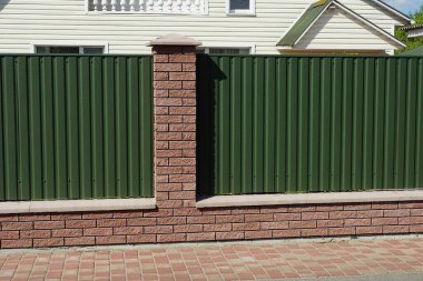 Kırsal bir sokaktaki kaldırımda kahverengi tuğlalardan ve yeşil metalden yapılmış bir çit parçası.