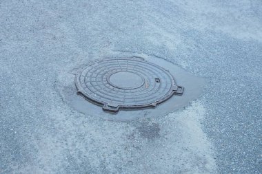 Caddedeki gri asfaltta kahverengi, nemli bir lağım çukuru var.