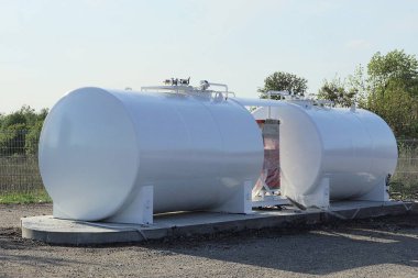 İki büyük endüstriyel metal varil bir benzin istasyonunda yol kenarındaki gri asfaltta duruyor.