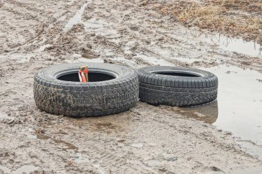 İki siyah eski kirli lastik, kahverengi toprakta, yoldaki suda yatıyordu.