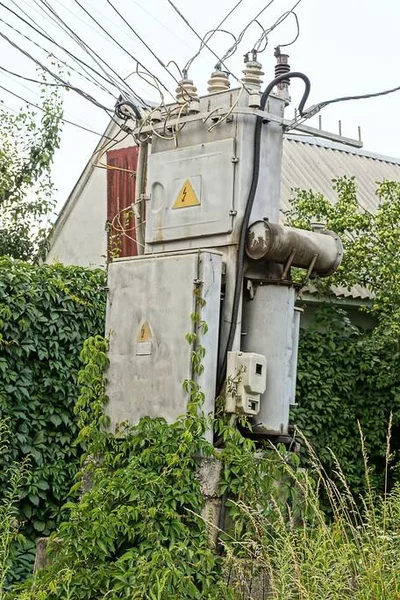 通りに緑の植生が生い茂る電線のある大きな灰色の鉄の変圧器の一つ — ストック写真