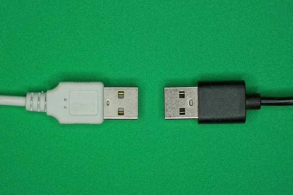 两根插有插头的黑色白色电缆躺在一张绿色桌子上 — 图库照片